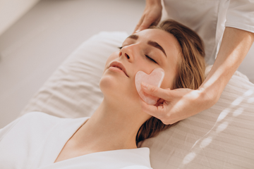 Woman receiving a facial massage with a rose quartz tool, promoting self-care and skincare rituals.